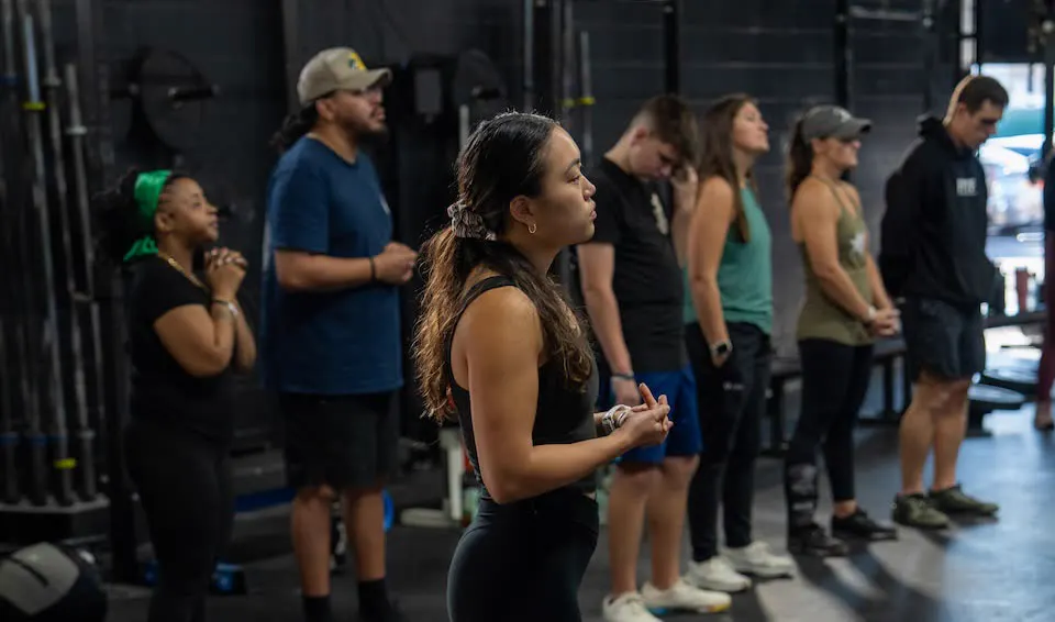 Gathering attendees standing in a gym, some with hands open in prayer