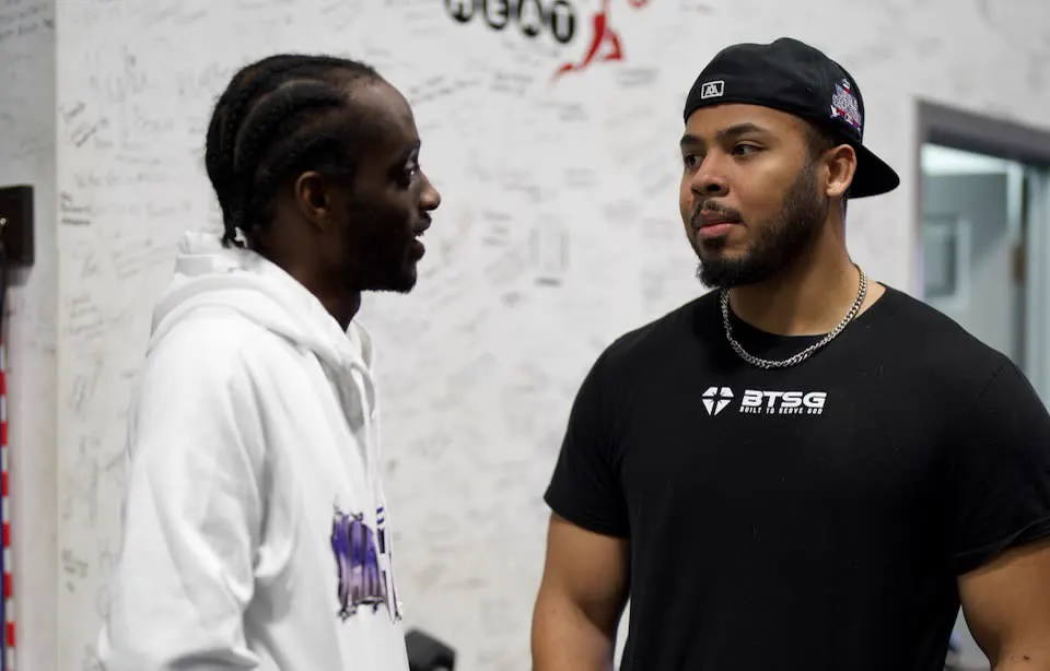 Two men talking in a gym, one wearing a black BTSG t-shirt